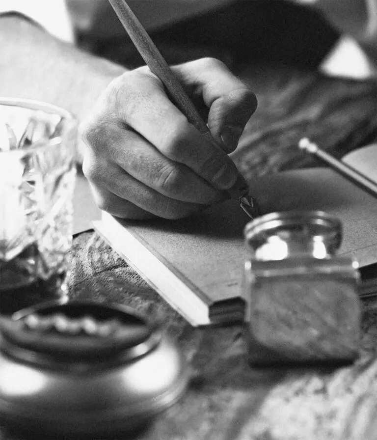 A black and white image of a person writing in a book using a calligraphy pen.