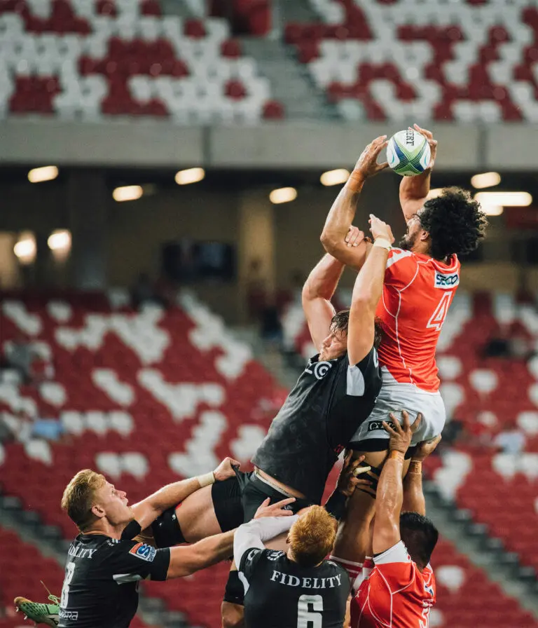 A still of a rugby match where a man catches the ball from a sideline throw in and other attempts to take it off him, whilst their teammates support them from beneath.