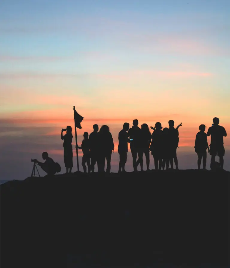 A group of people stand at a summit, silhouetted against a setting sun.