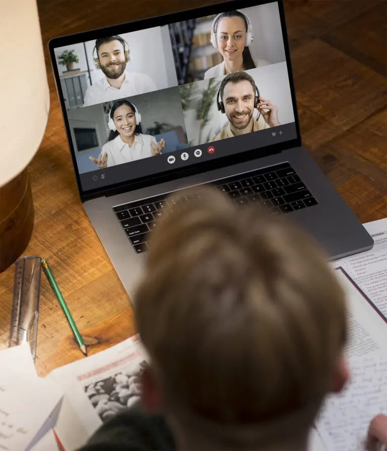 A person is on a zoom call with 4 people on a laptop with study books around them on a wooden table.