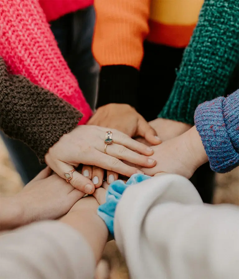 A group of people lay their hands on top of each other in a circle in a 'hands in' action.